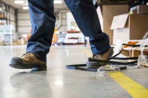 An industrial safety topic. A worker tripping over a trash on a factory floor cm 300x200