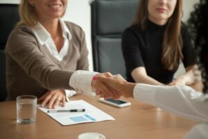 Diverse businesswomen shaking hands at group meeting or job interview cm 300x200